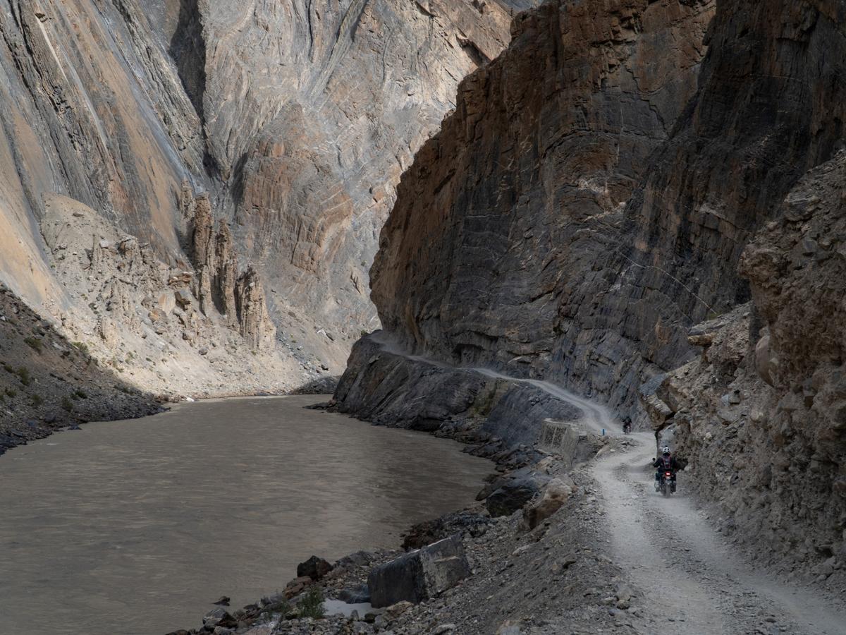 A group of motorcyclists riding through a narrow, rocky mountain pass with a river running through it
