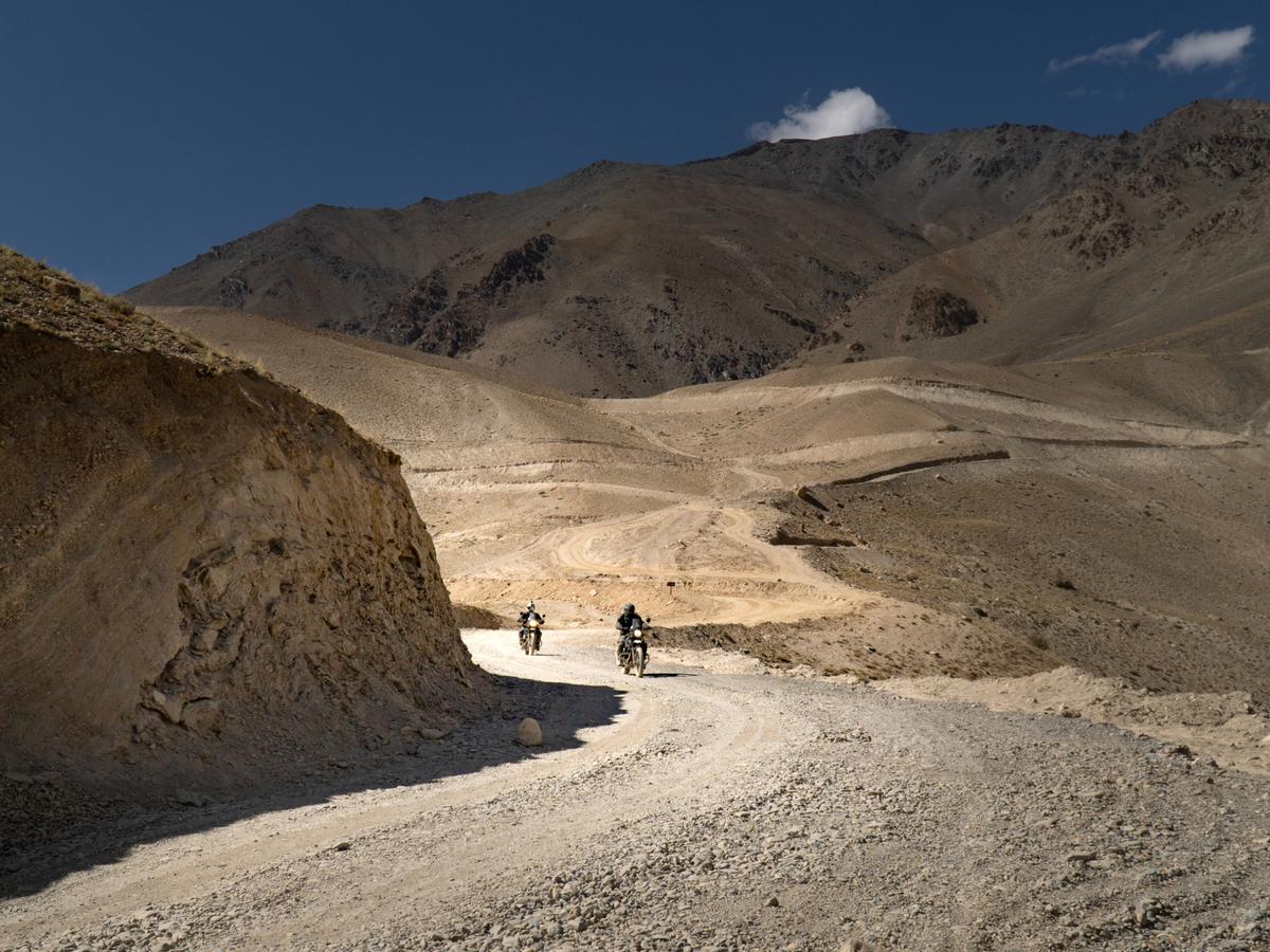 Two motorcyclists riding through a mountainous region on a dirt road