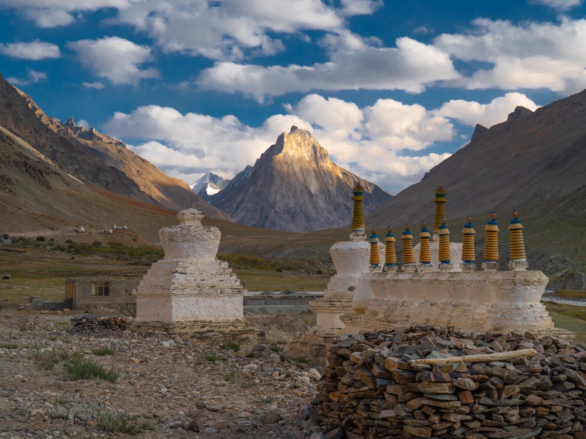 A group of white and gold Buddhist monasteries in the Himalayas, with a snow-capped mountain in the background.