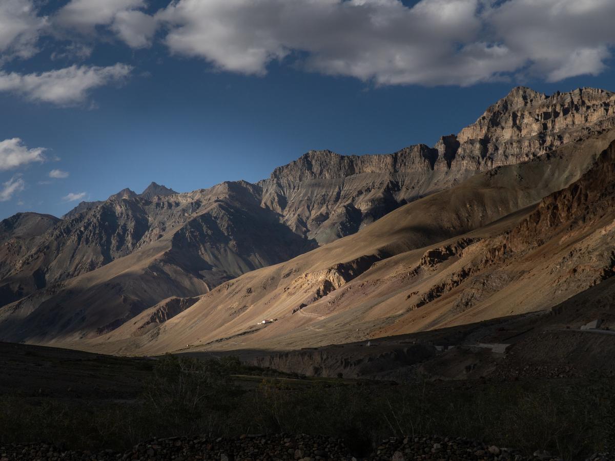 A mountainous landscape with a mix of brown and green vegetation, under a blue sky with white clouds.