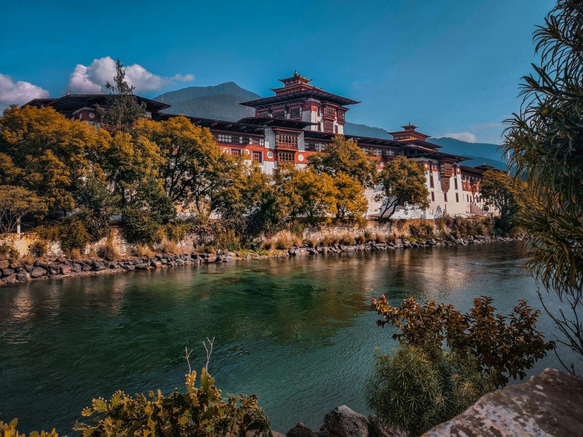 A Bhutanese monastery perched on the banks of a river, with a mountain range in the background