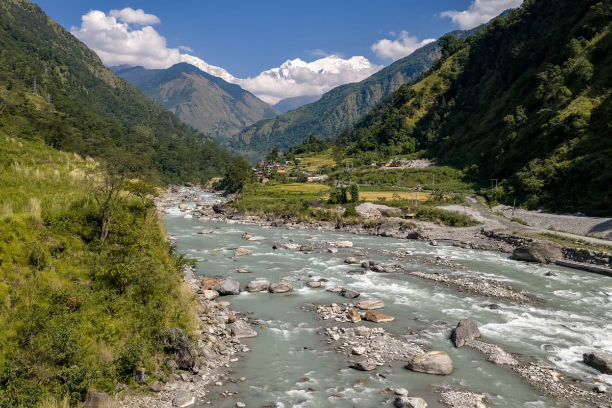 Rocky river flowing through a lush valley with terraced fields and mountains in Nepal during our Chris Birch Signature tour.