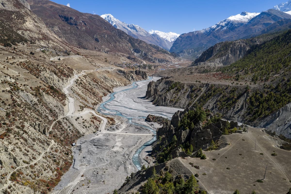 Aerial view of a winding river valley with terraced slopes and snow-capped mountains in the background during our Nepal motorcycle tour.