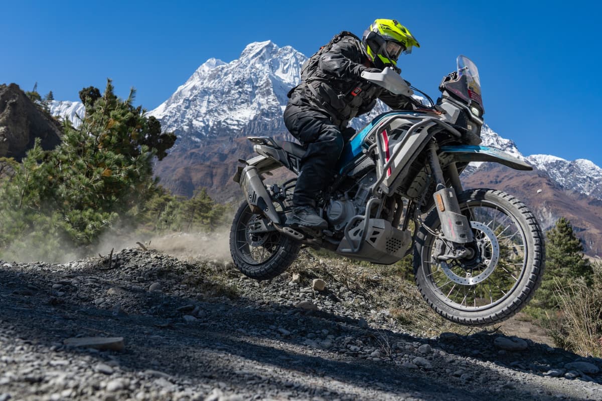 Motorcyclist performing a wheelie on a dirt trail with snow-capped mountains in the background during our Nepal motorcycle tour.
