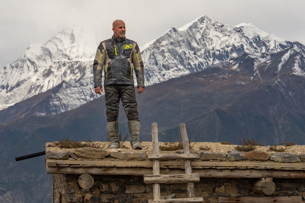 Man in motorcycle riding gear standing on a rustic rooftop with snow-capped mountains in the background during our Nepal motorcycle tour.