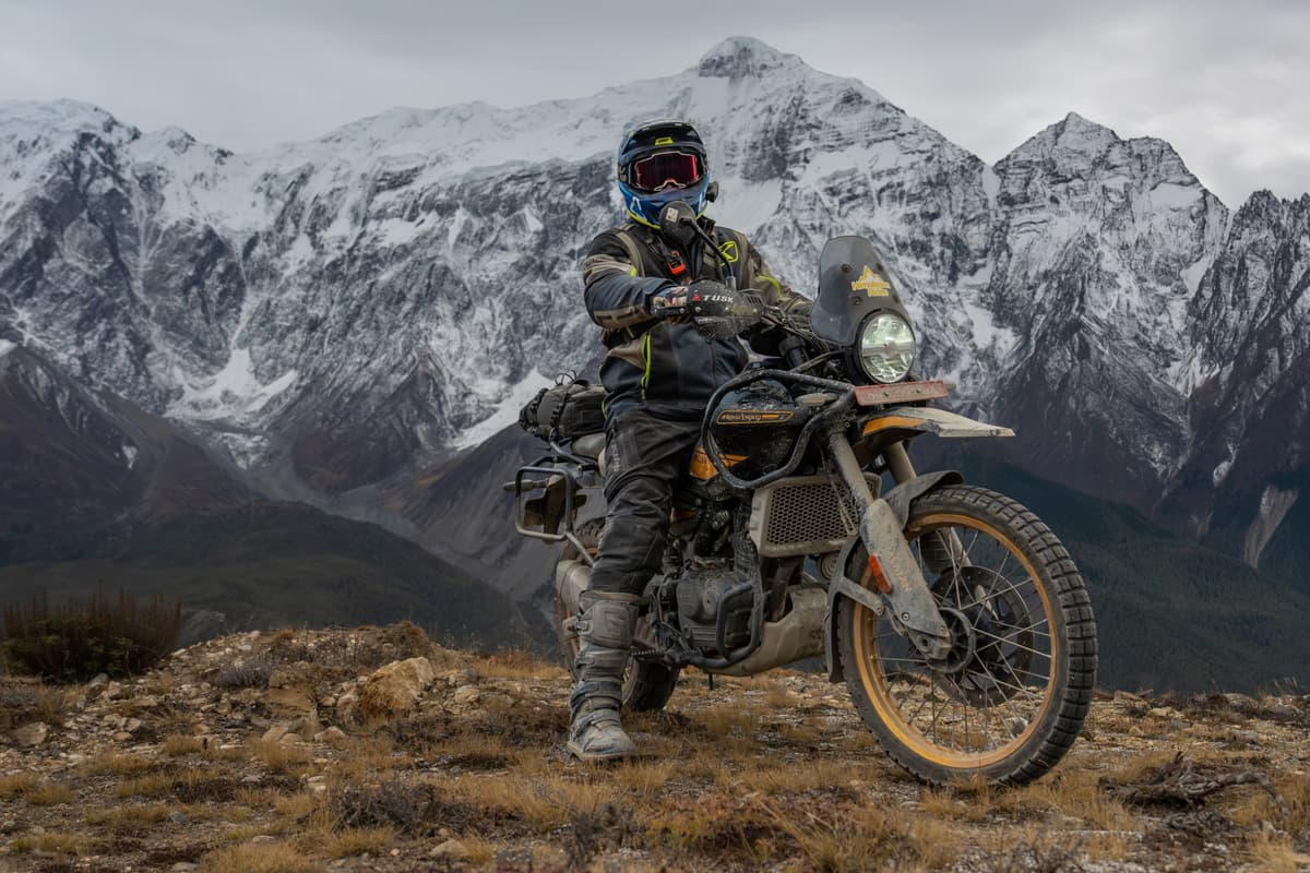 Motorcyclist standing beside adventure motorcycle during our Nepal motorcycle tour with dramatic snow-capped mountains in the background.