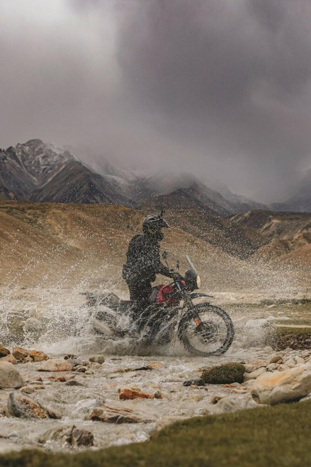 a rider splashes through a stream on an adventure motorcycle in nepal.