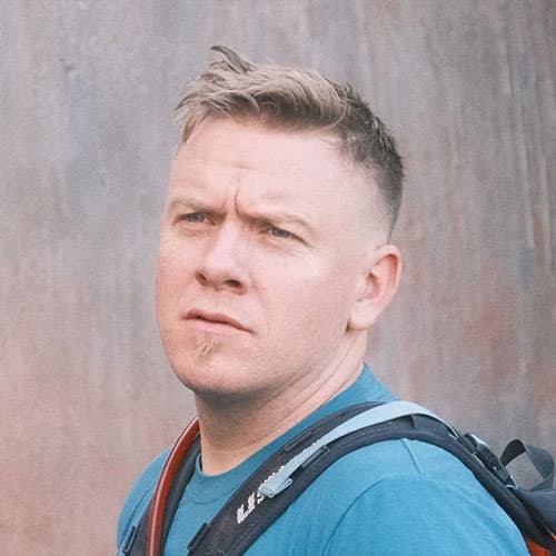 Portrait of Ryan H wearing a blue shirt with a backpack strap, looking off to the side during our motorcycle tour.