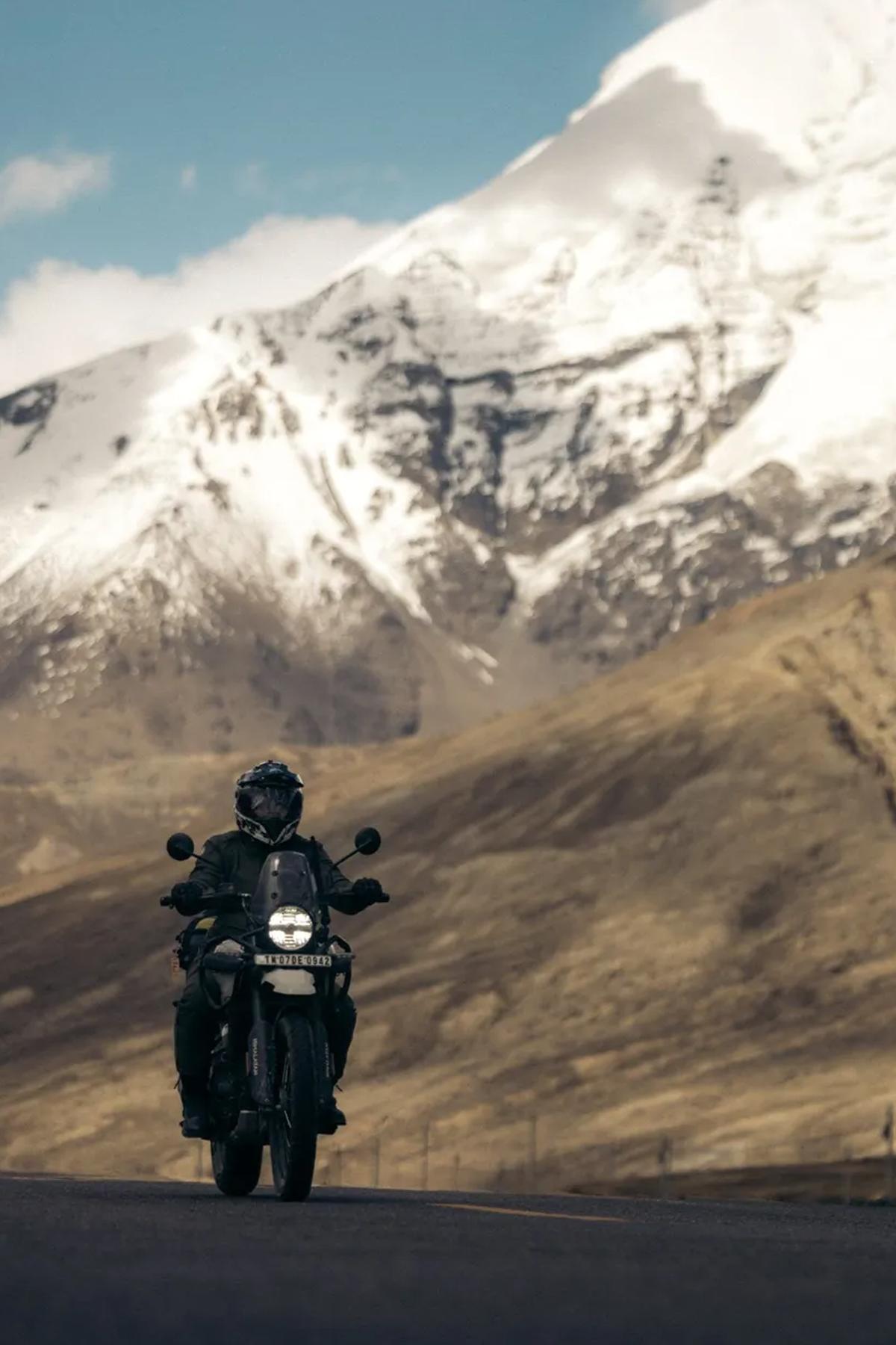 a person on a motorcycle riding on a mountain road with snow-capped mountains in the background